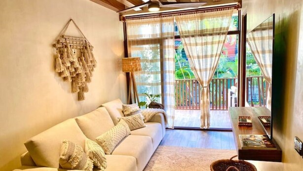 A living room with a beige sofa, a woven basket, and a view of a balcony with a wooden railing. - Beautiful apartment with pool (Sayulita)