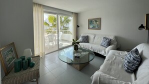 A modern living room with a glass coffee table, white sofa, and a balcony with outdoor furniture. - ISholidays Acron Puerto Pollensa (Port de Pollença)