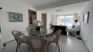 A dining area with a glass table surrounded by wicker chairs, a potted orchid, and a view of a balcony with a bed and a lamp. - ISholidays Acron Puerto Pollensa (Port de Pollença)