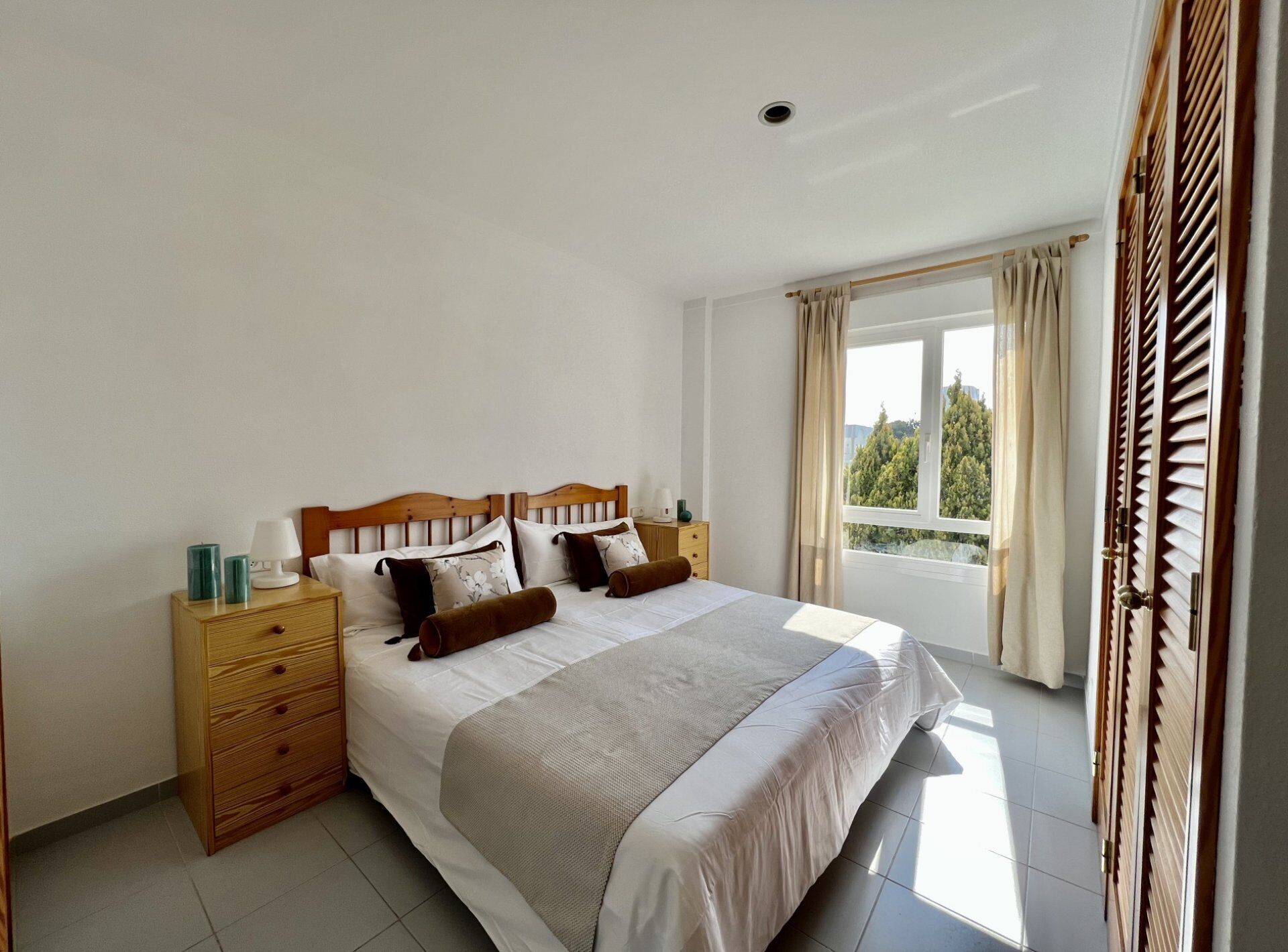 A bedroom with a large bed, wooden headboard, bedside tables, and a window with curtains.