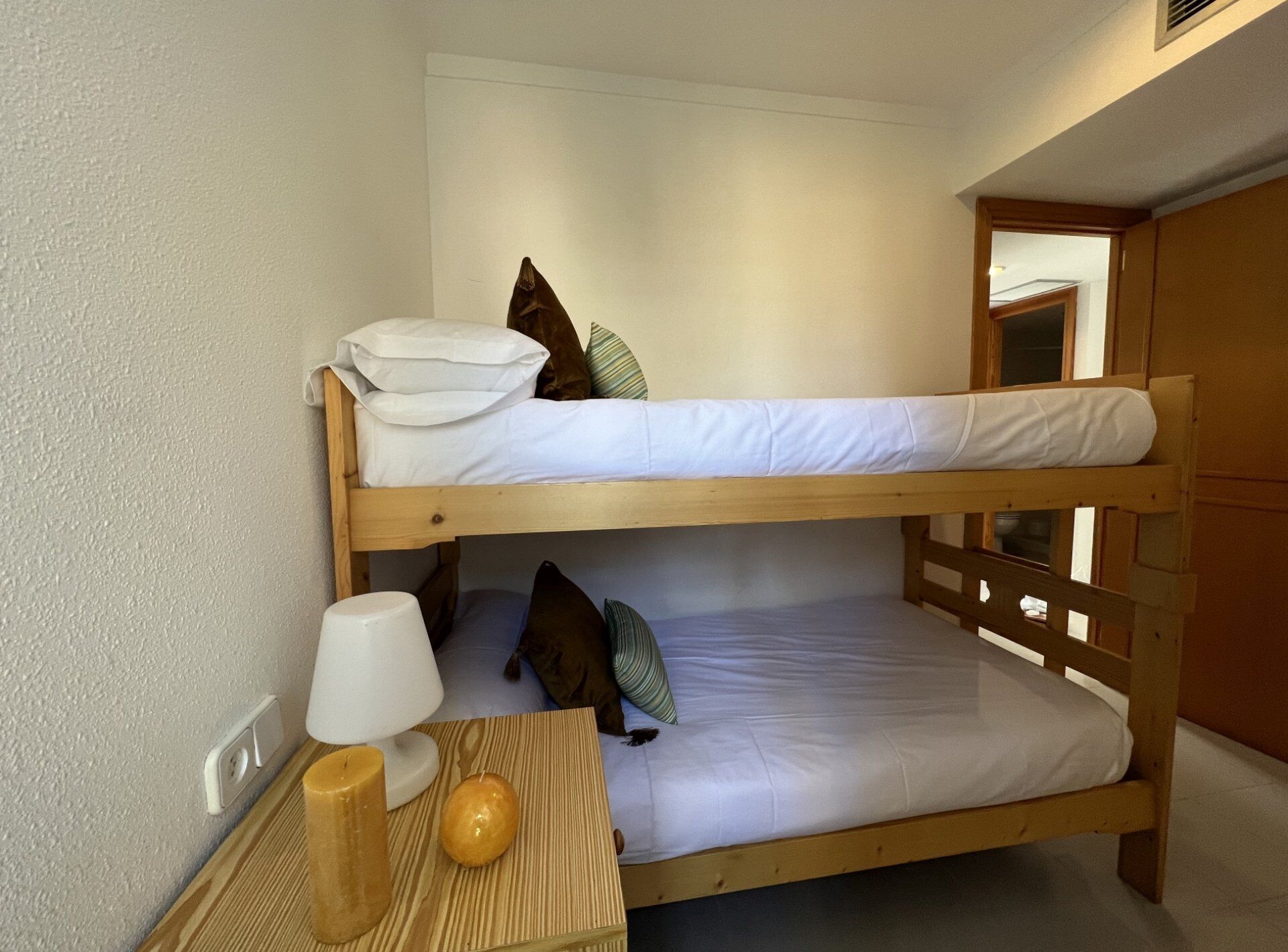 A bunk bed with white bedding, a bedside lamp, a candle, and a wooden tray.