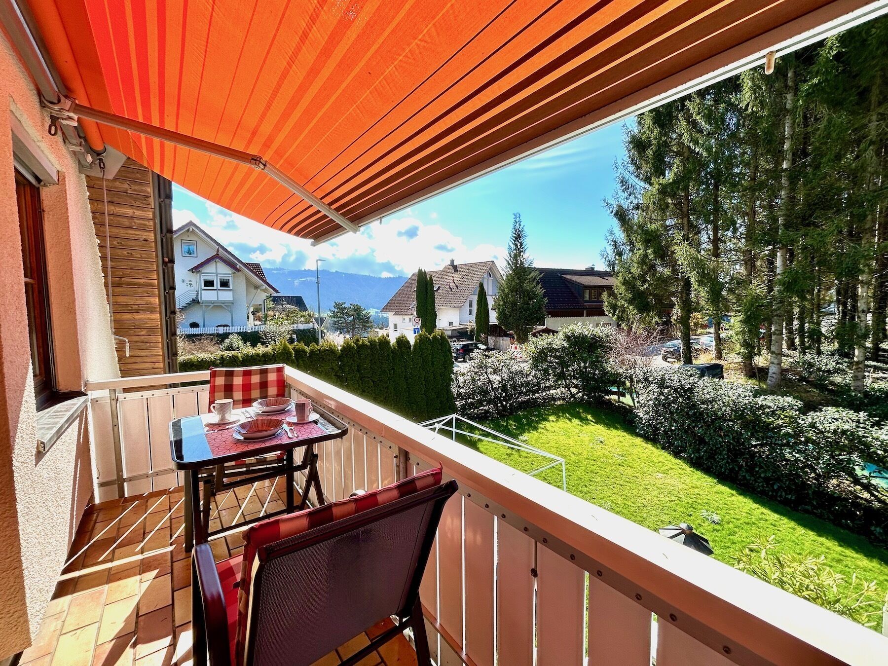 Un balcón con mesa y sillas, con vistas a un jardín cuidado y una zona residencial.