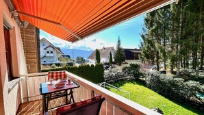 Un balcon avec une table et des chaises, donnant sur un jardin bien entretenu et un quartier résidentiel.