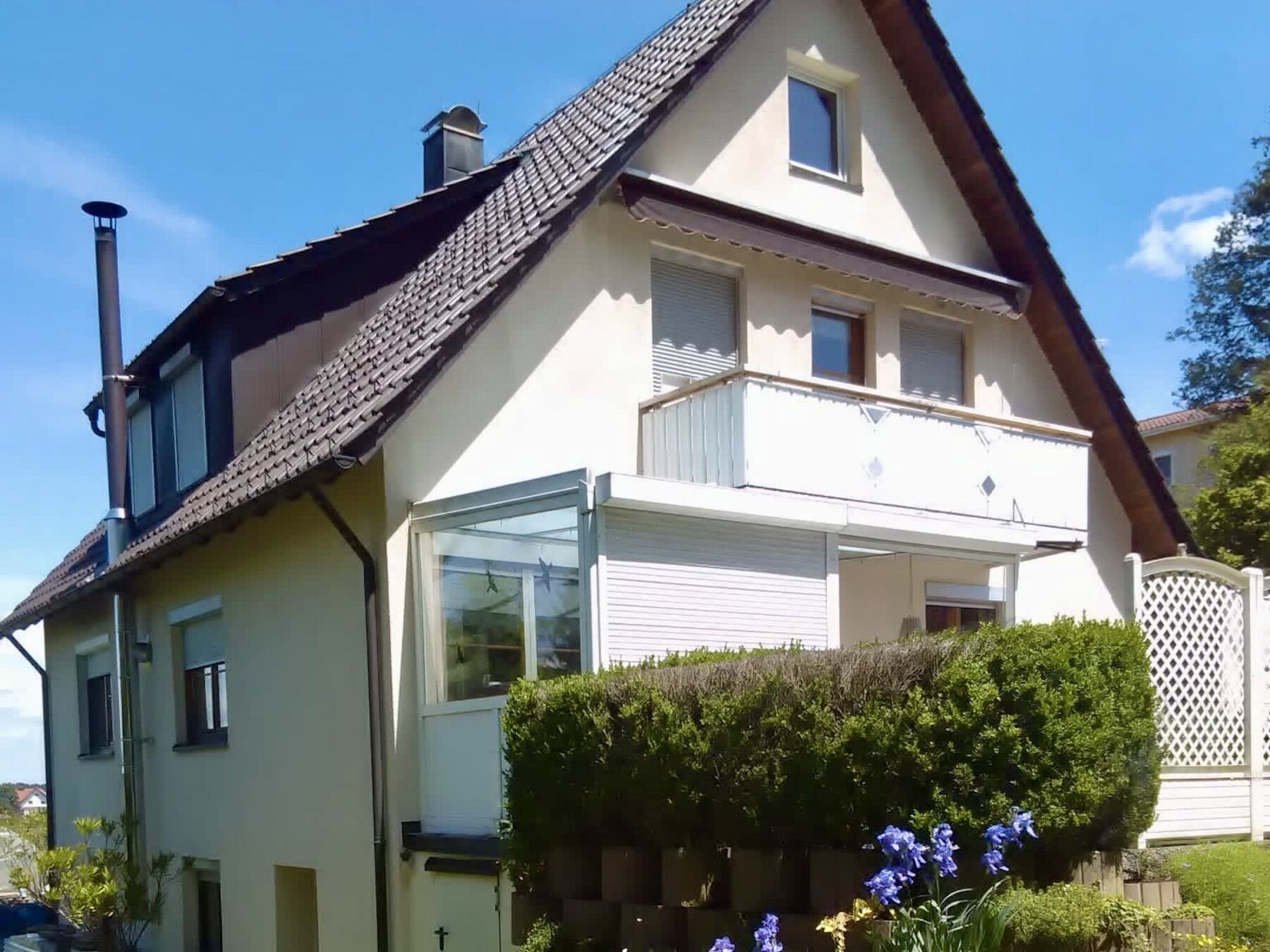 A two-story house with a sloped roof, a chimney, and a balcony with a white railing.