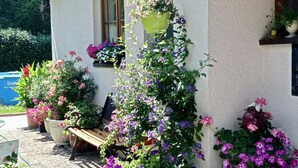 Une maison à l’extérieur blanc, avec un banc en bois, ainsi que divers pots de plantes et de fleurs.
