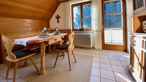 Un coin repas chaleureux avec des murs en bois, une table dressée pour deux personnes et un radiateur placé sous une fenêtre.