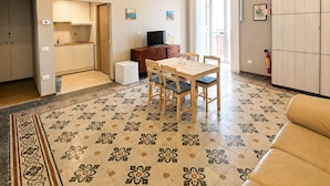Un amplio salón con una mesa de comedor, sofá, cocina y suelo estampado.