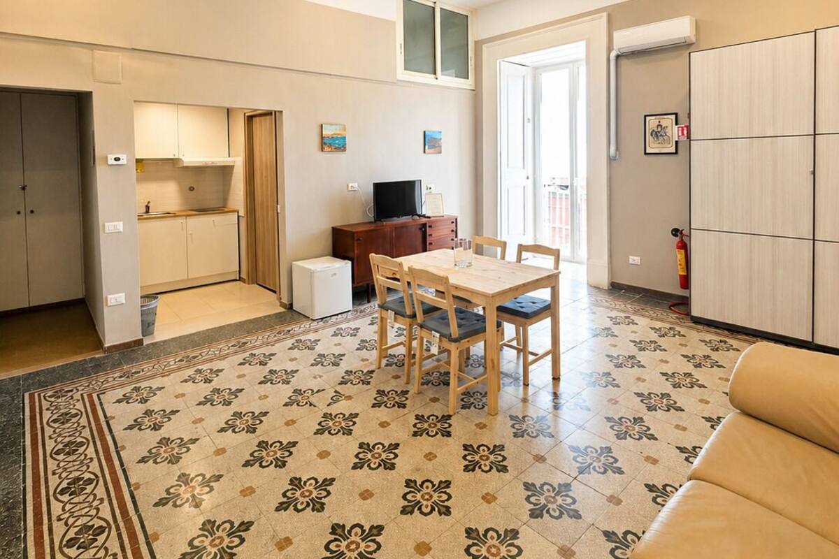 A spacious living area with a dining table, sofa, kitchen, and a patterned floor.