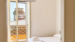 Un dormitorio con cama, lámpara colgante, piso de baldosas y vista a un edificio a través de una puerta de cristal.