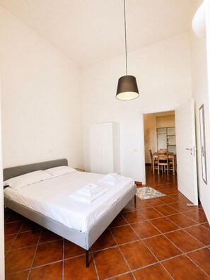 A bedroom with a bed, a wardrobe, a dining table with chairs, and a hanging light fixture. - Chocolate's Home (Naples)