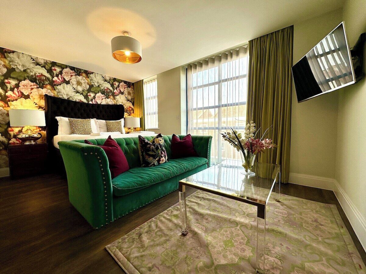 A living room with a green sofa, a glass coffee table, and a floral wallpaper.