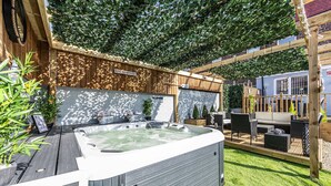 Een hottub met een houten terras, omringd door een houten omheining en begroeiing.