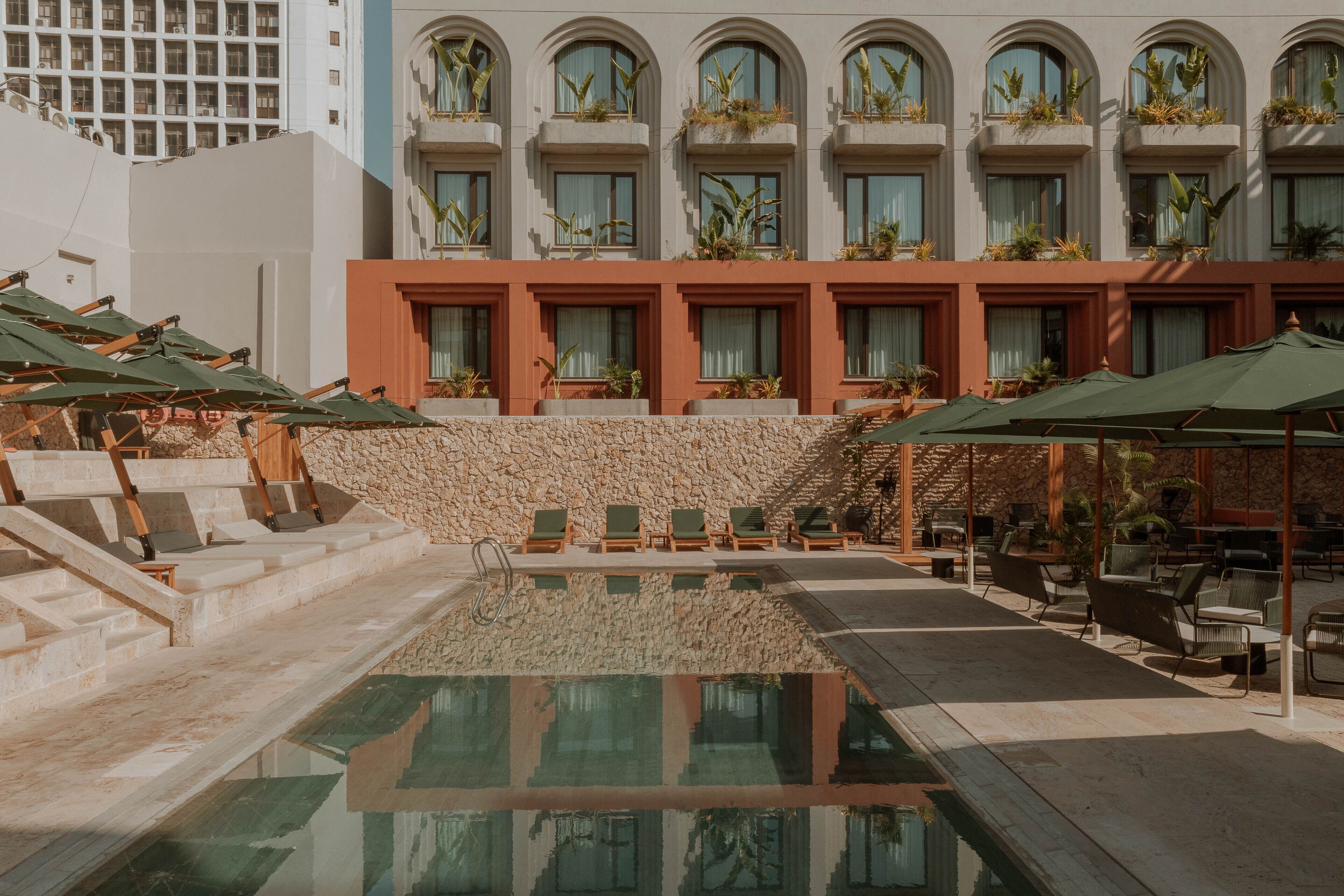 A hotel pool area with a stone wall, lounge chairs, and umbrellas.