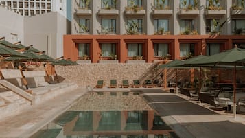 A hotel pool area with a stone wall, lounge chairs, and umbrellas.