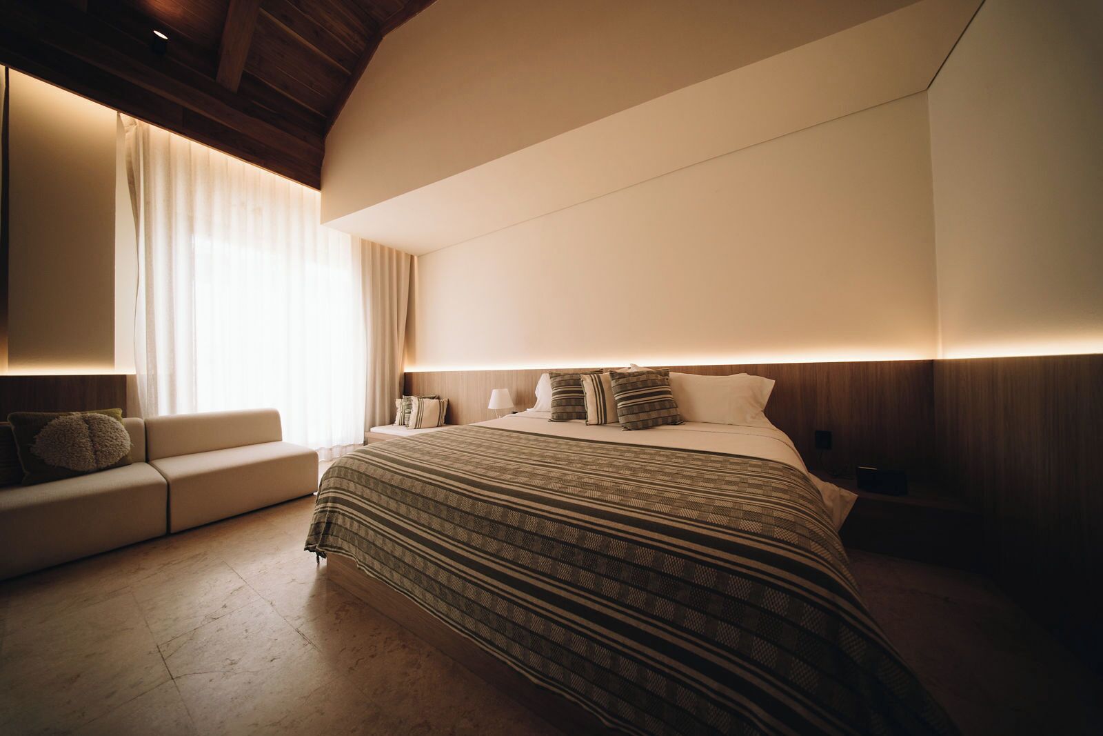 Une chambre d’hôtel moderne avec un grand lit, un canapé et un plafond en bois.