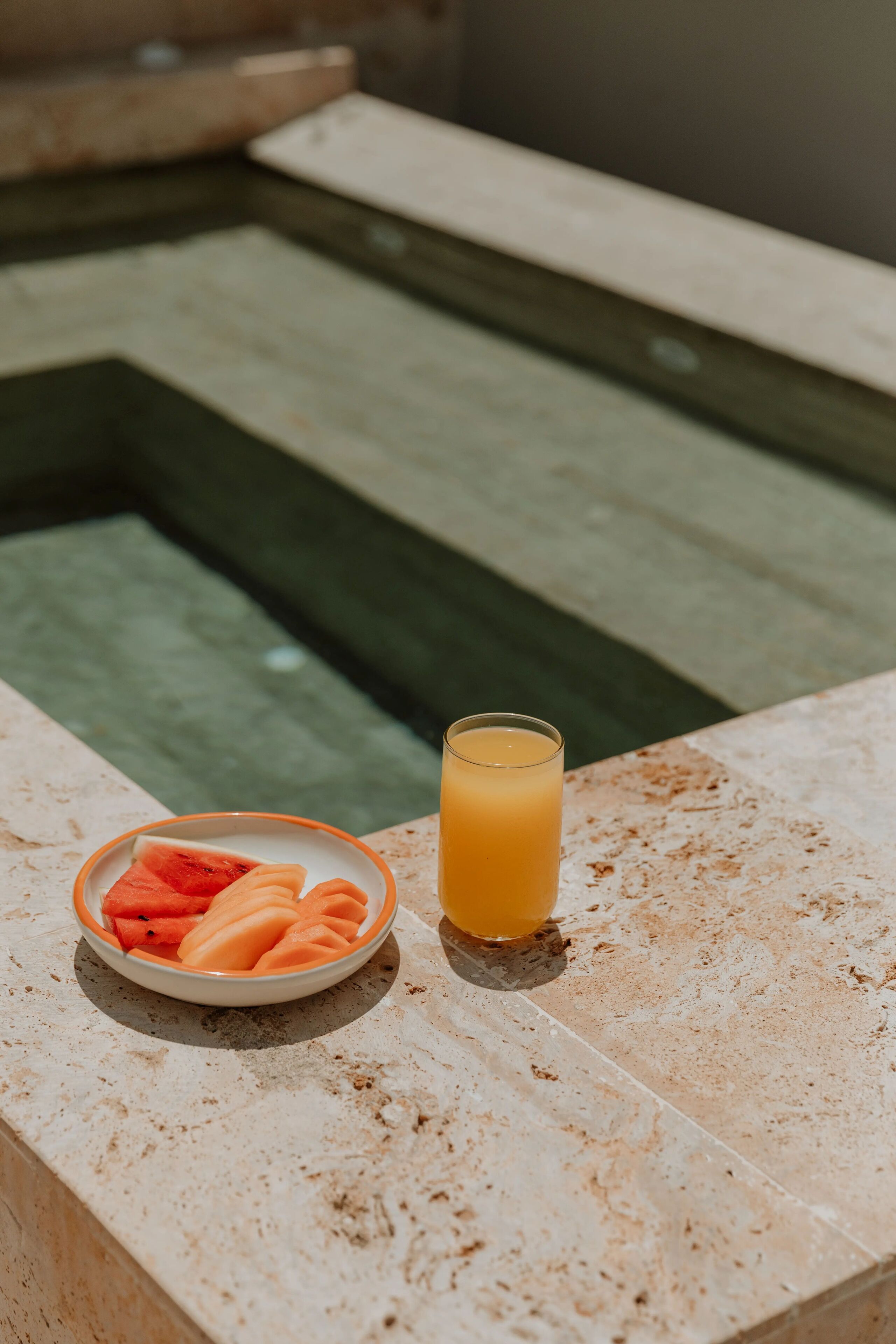 A marble countertop with a bowl of watermelon slices and a glass of orange juice.