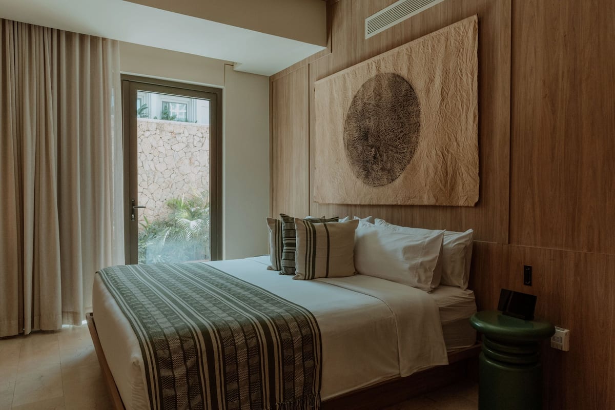 A hotel room with a bed, curtains, a large wall art piece, and a view of the outdoors.