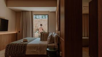 A modern hotel room with a large bed, a bedside table, a TV mounted on the wall, and a view of the outside balcony.
