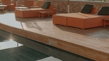 A sunlit outdoor seating area with orange sofas and a wooden deck.