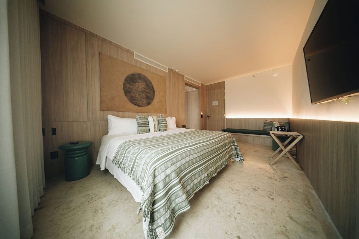 A hotel room with a bed, a wall-mounted TV, a wooden headboard, and a large circular artwork.