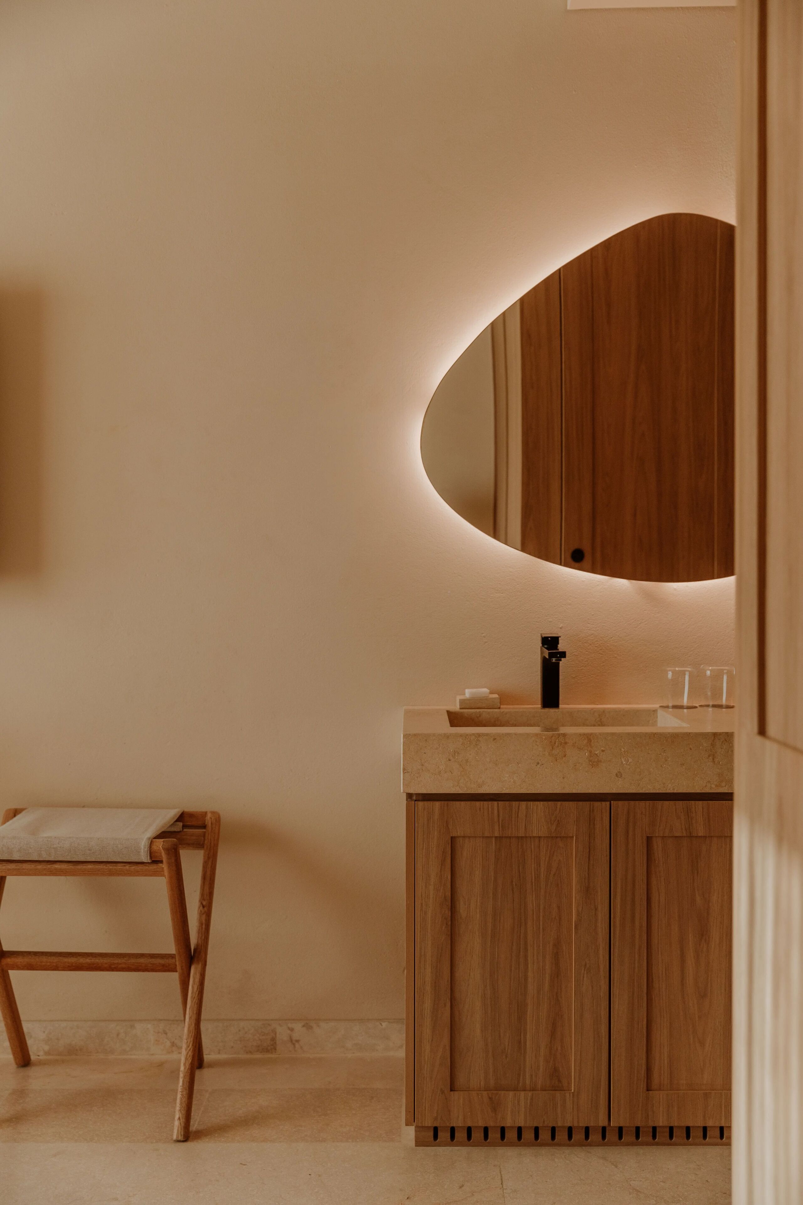 Un baño con tocador de madera, un espejo redondo y una silla de madera.