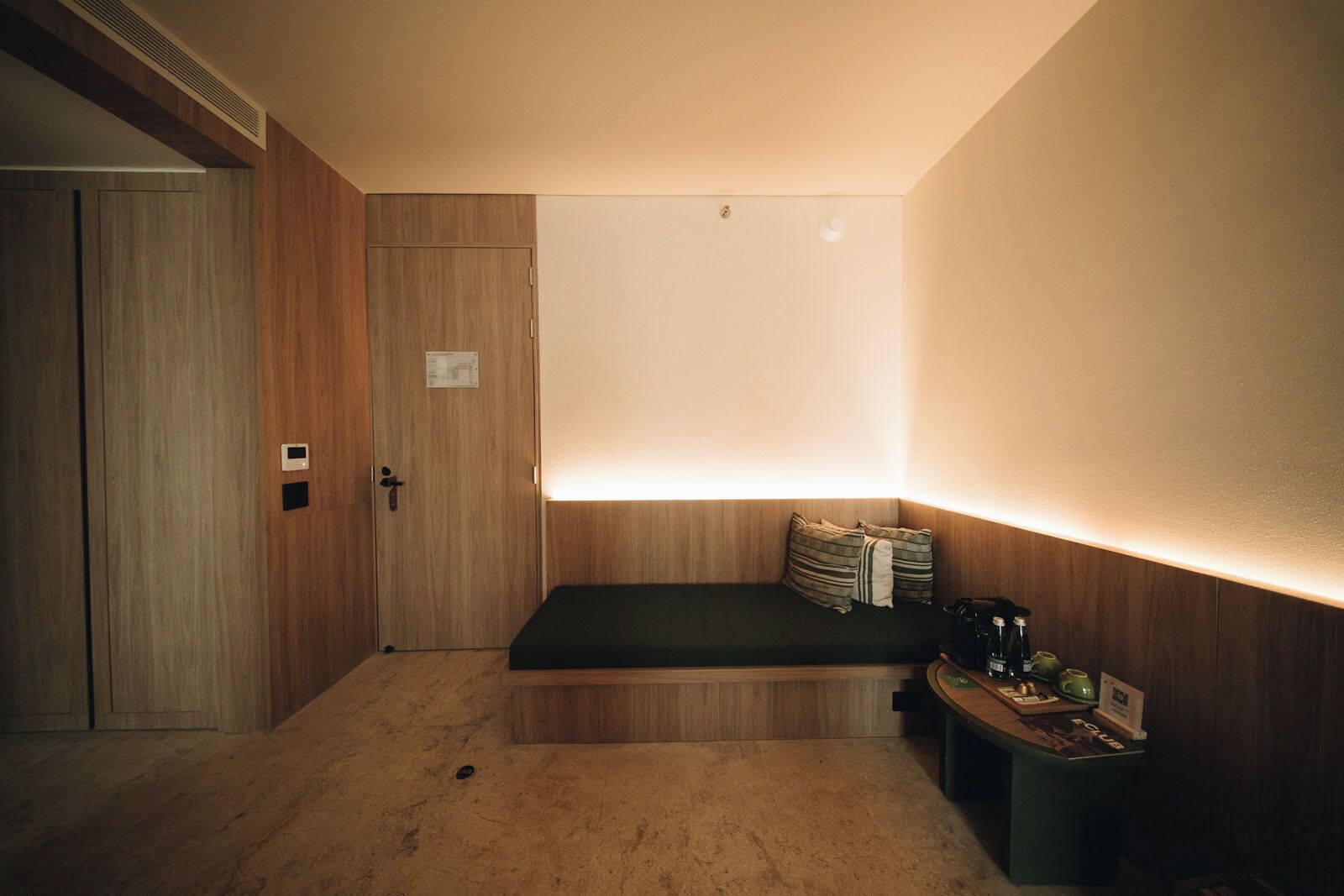 Une pièce comprenant une armoire en bois, un banc avec des coussins, une petite table avec une machine à café et un luminaire fixé au mur.