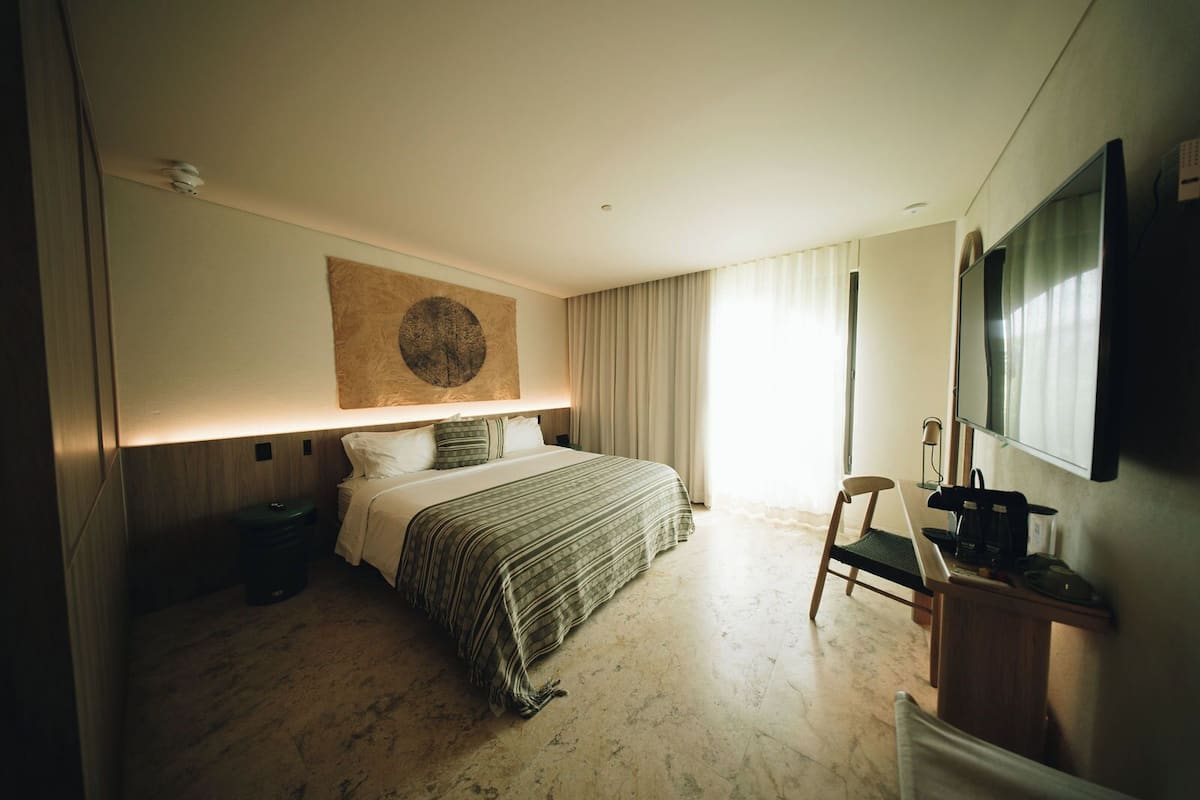 A hotel room with a bed, a desk with a chair, a flat-screen TV, and a large artwork on the wall.