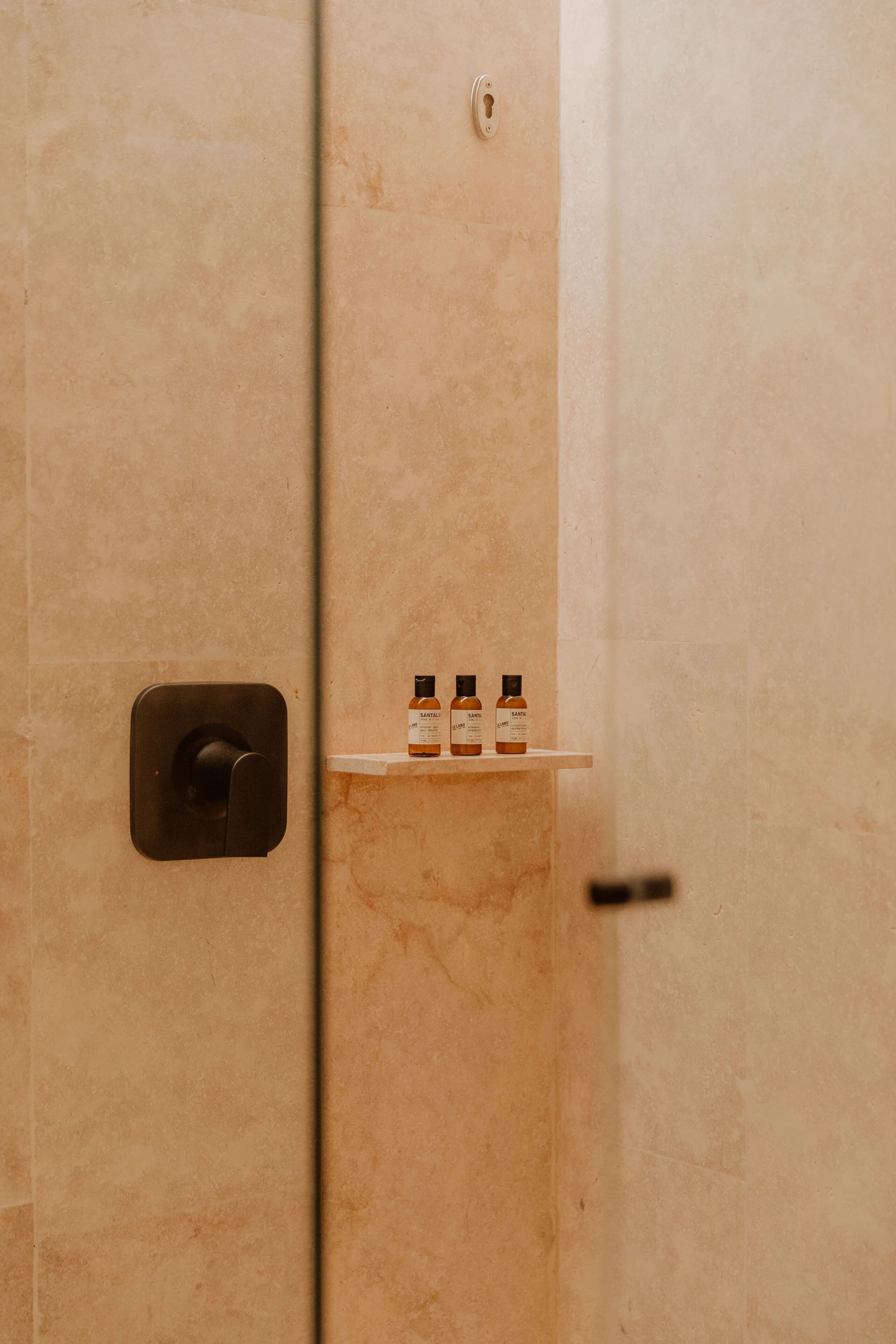 A bathroom with a marble wall, a towel rack, and three bottles of shampoo.