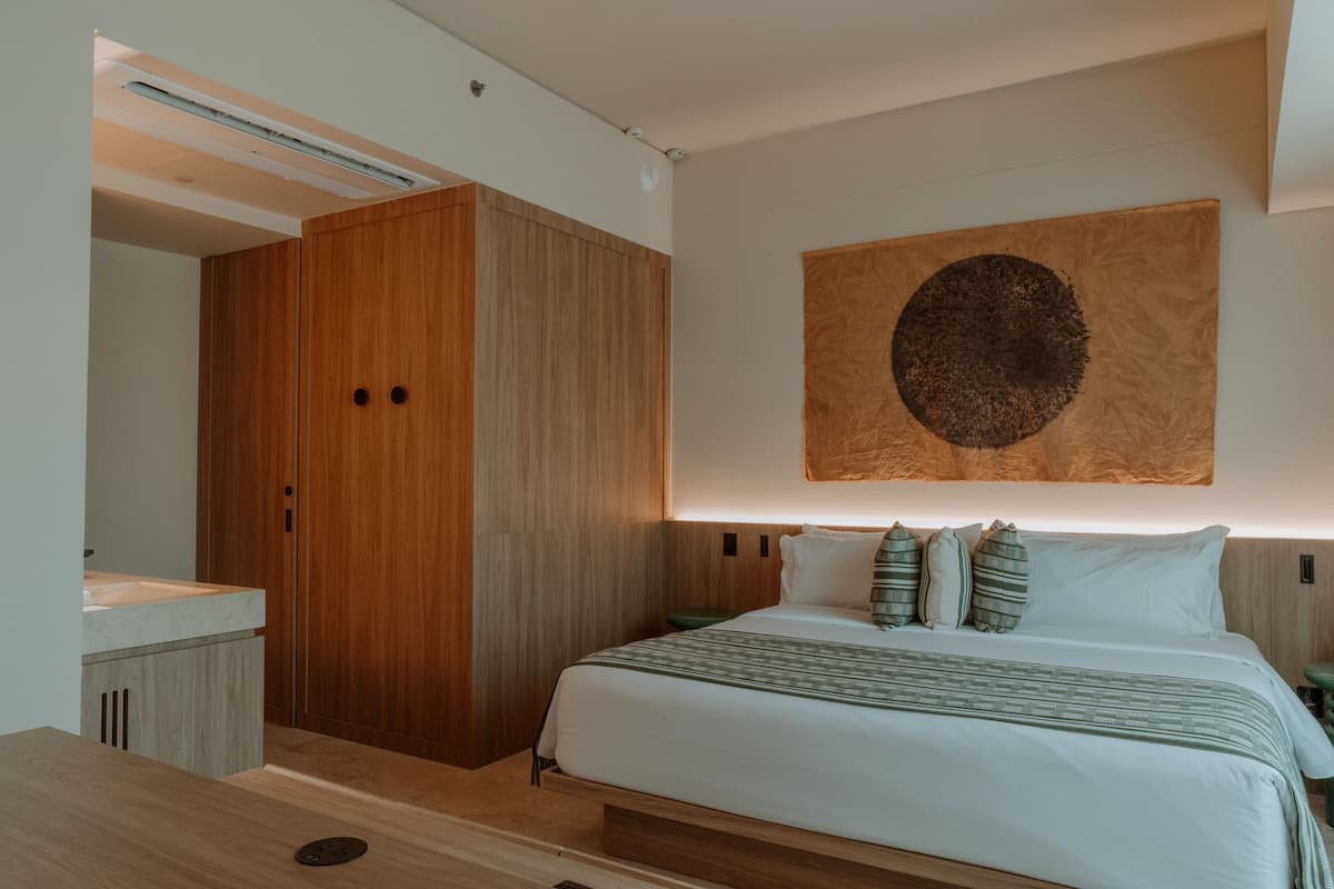 A modern bedroom with a wooden wardrobe, a large bed with multiple pillows, and a unique circular artwork on the wall.