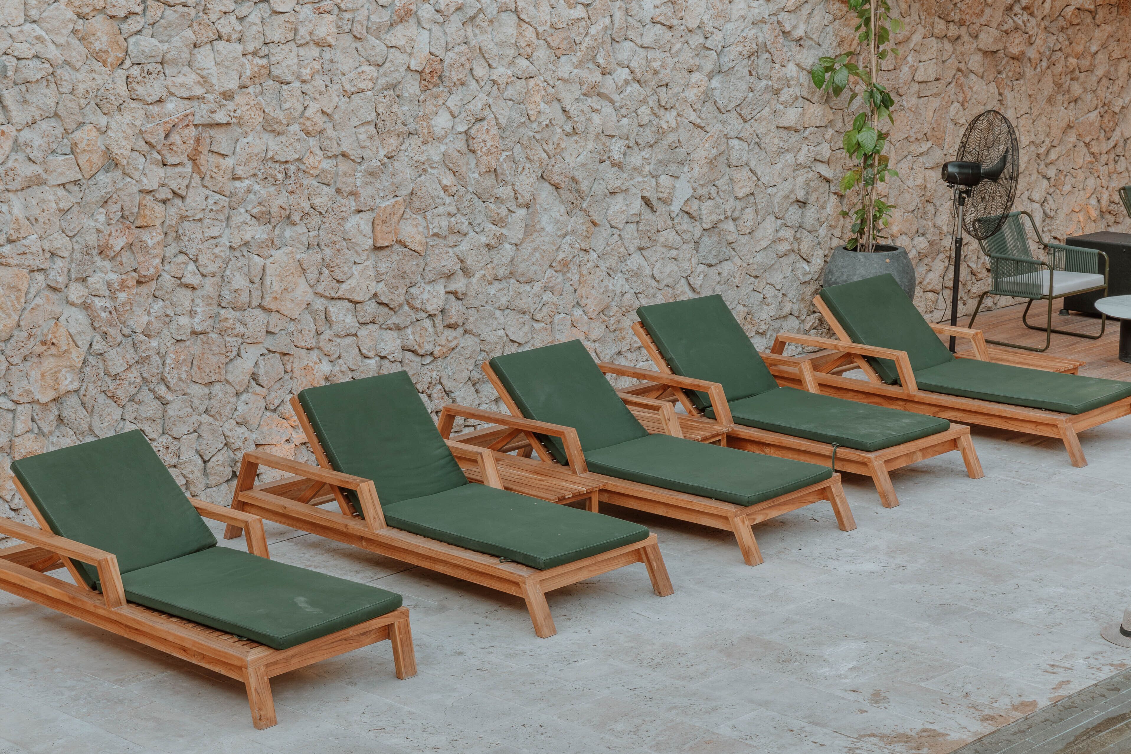 Filas de sillones de madera con cojines verdes frente a una pared de piedra.