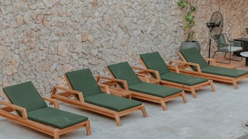 Filas de sillones de madera con cojines verdes frente a una pared de piedra.