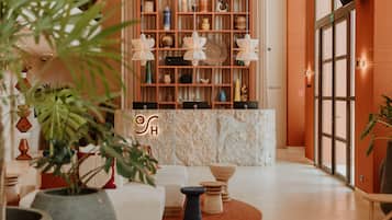 Um lobby moderno com uma receção de mármore, estantes com objetos decorativos e uma área de estar com um sofá e mesinhas laterais.
