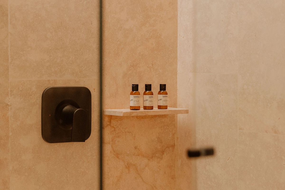 A bathroom with a marble wall, a towel rack, and three bottles of shampoo.