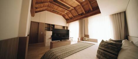 A bedroom with a large bed, a TV, wooden ceiling beams, and a window with curtains.