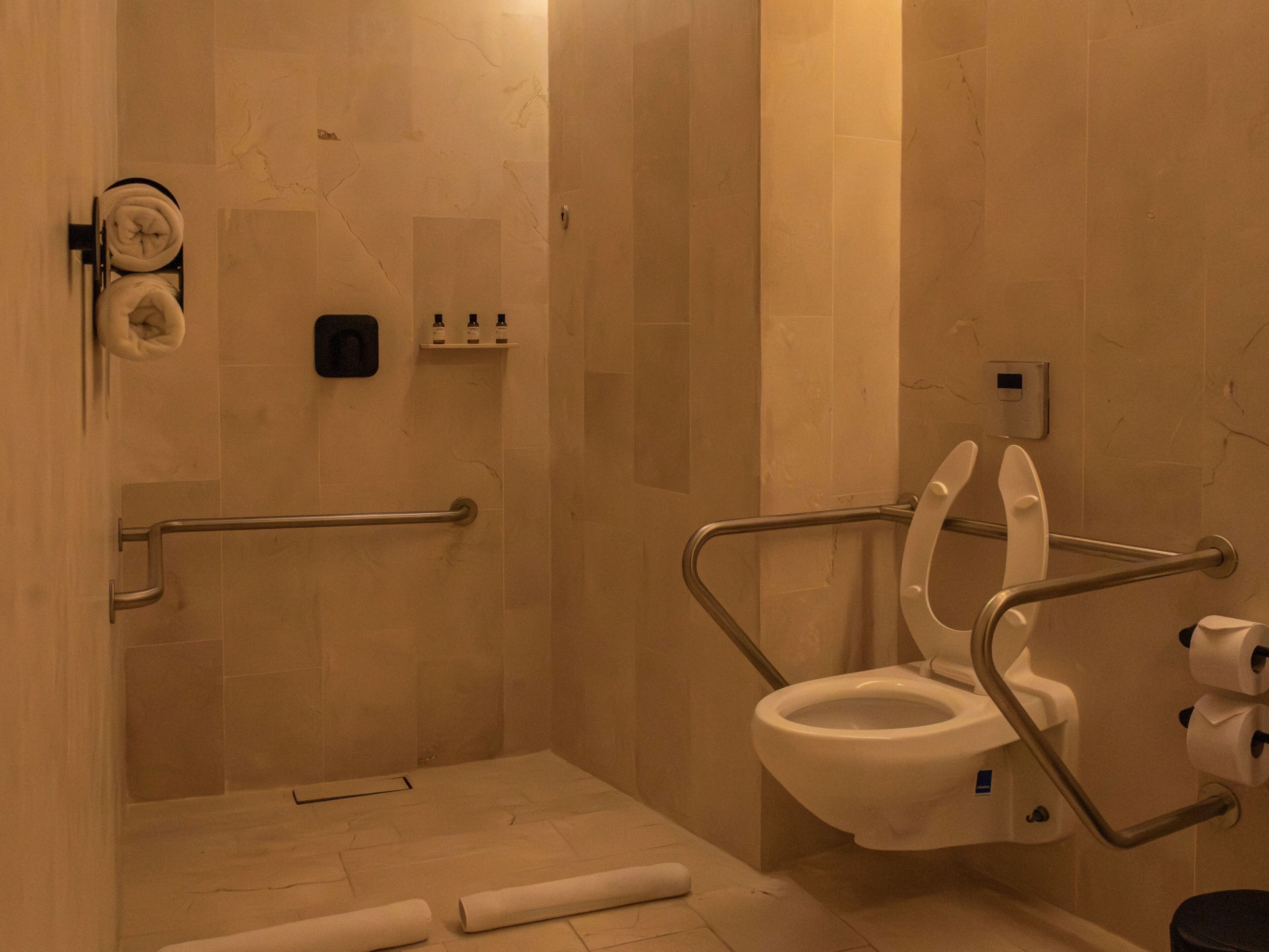 A handicap-accessible bathroom with a toilet, handrails, a towel dispenser, and a hand dryer.