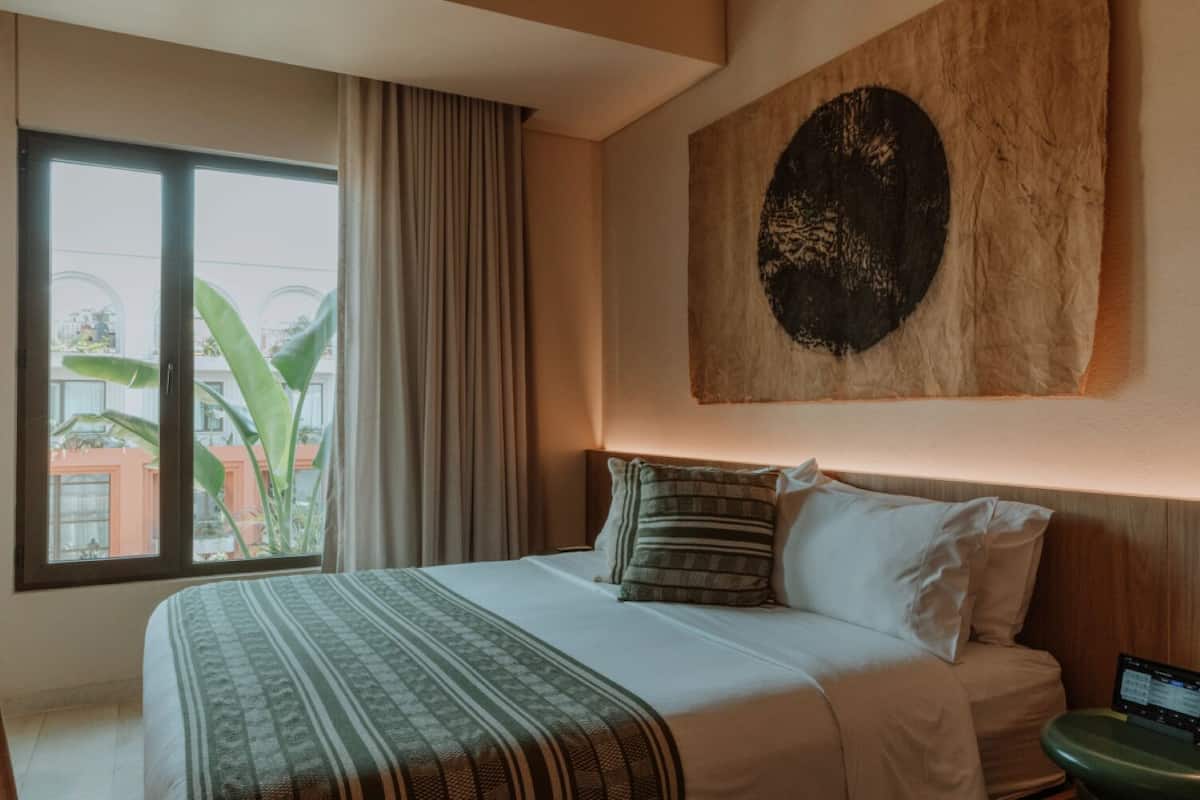 A hotel room with a large bed, a view of the outside, and a painting on the wall.