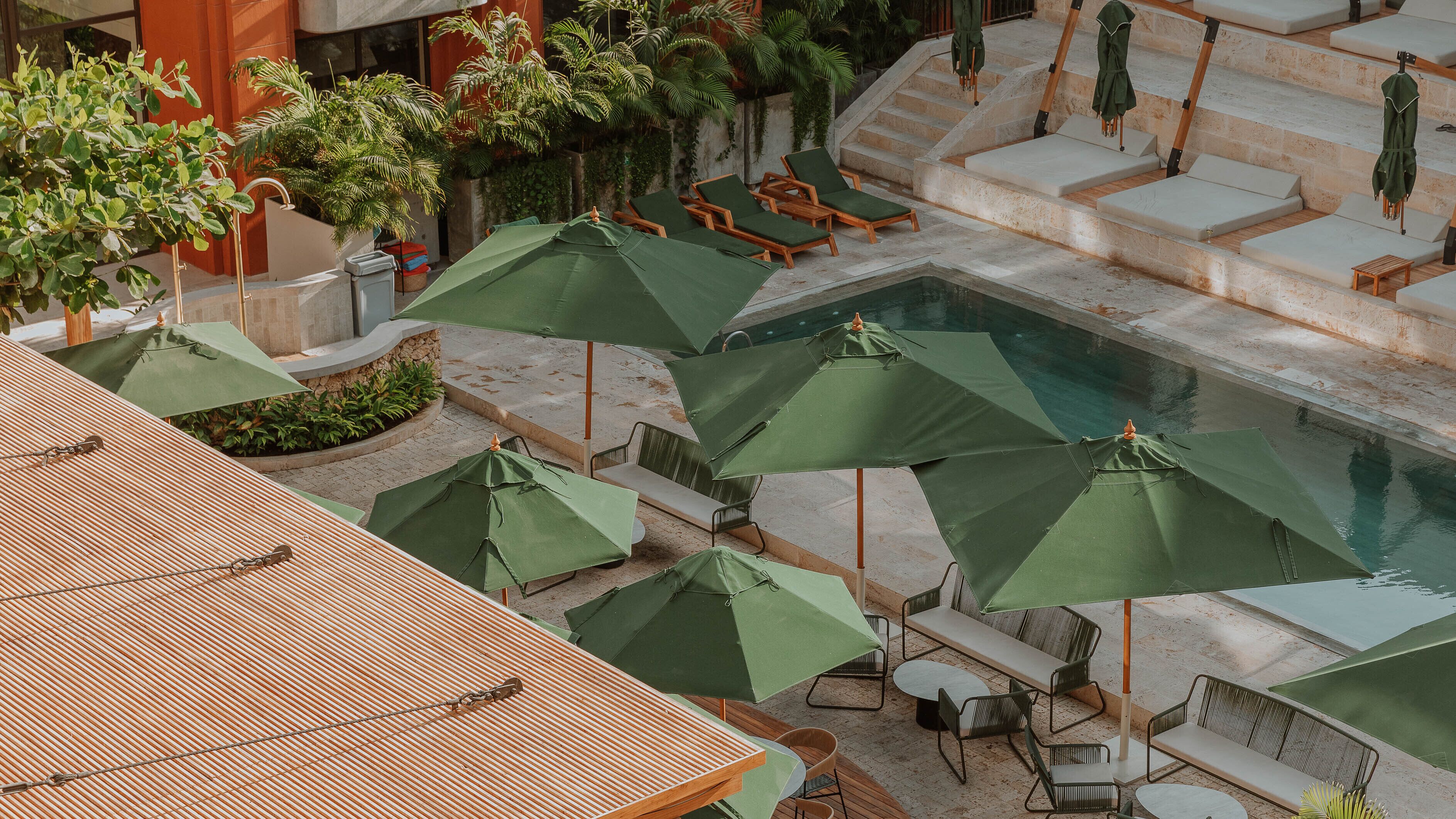 Un área de piscina en la azotea con varias sillas de descanso y sombrillas verdes.