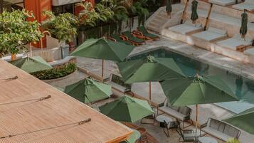 Un área de piscina en la azotea con varias sillas de descanso y sombrillas verdes.