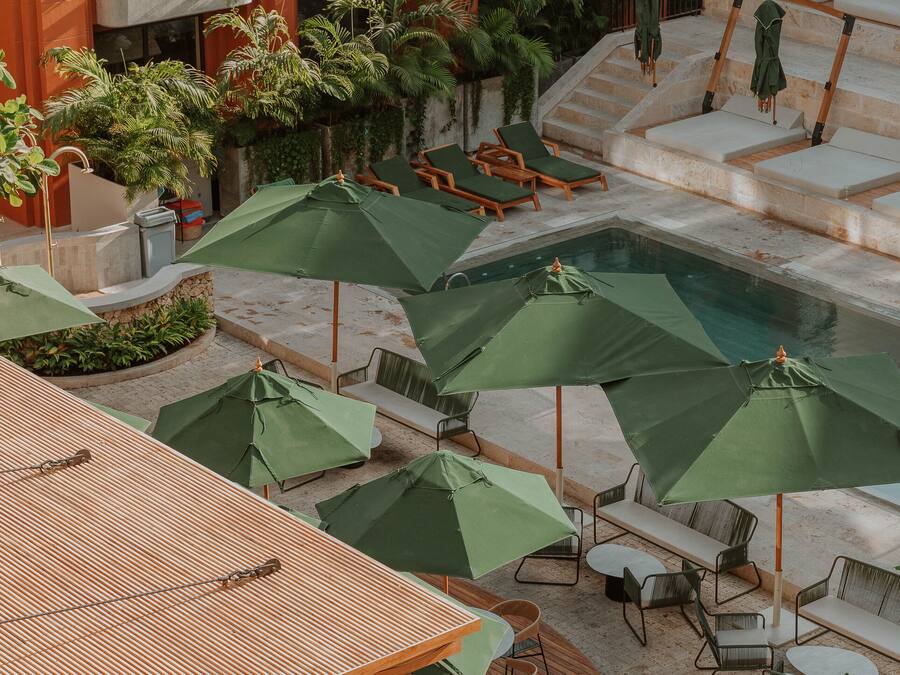 Un área de piscina en la azotea con varias sillas de descanso y sombrillas verdes.