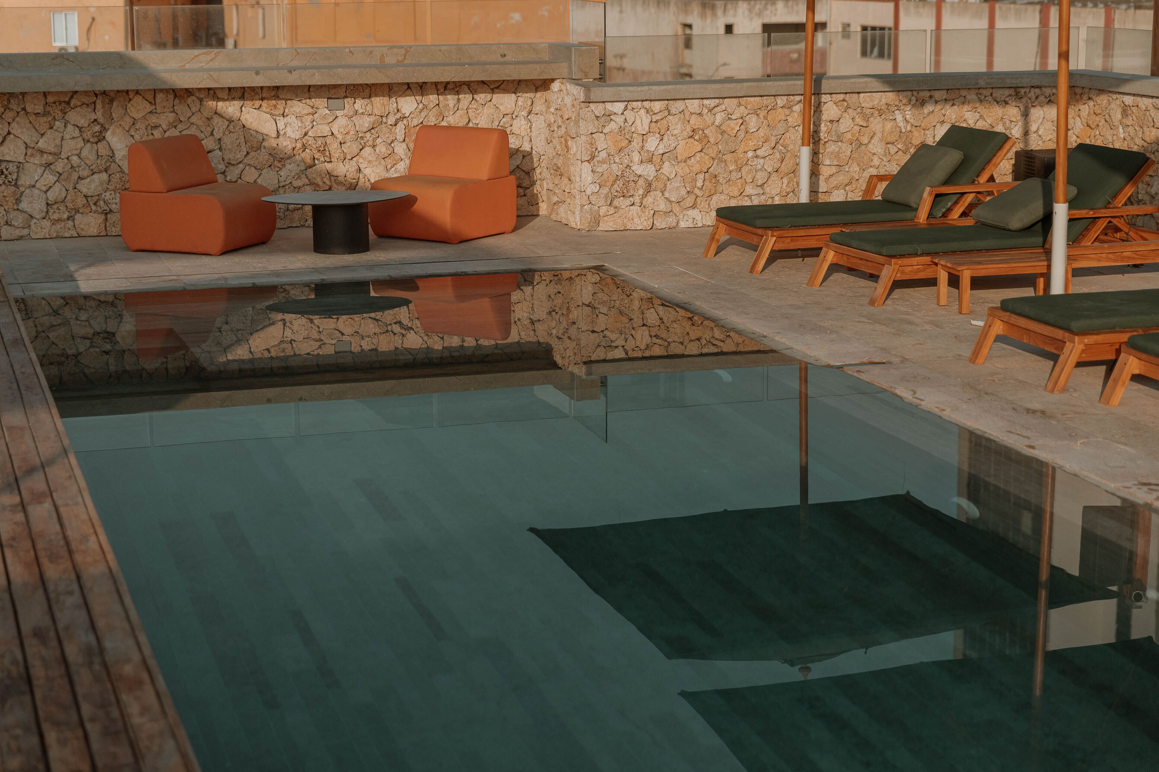 A pool area with lounge chairs and a table, surrounded by stone walls.