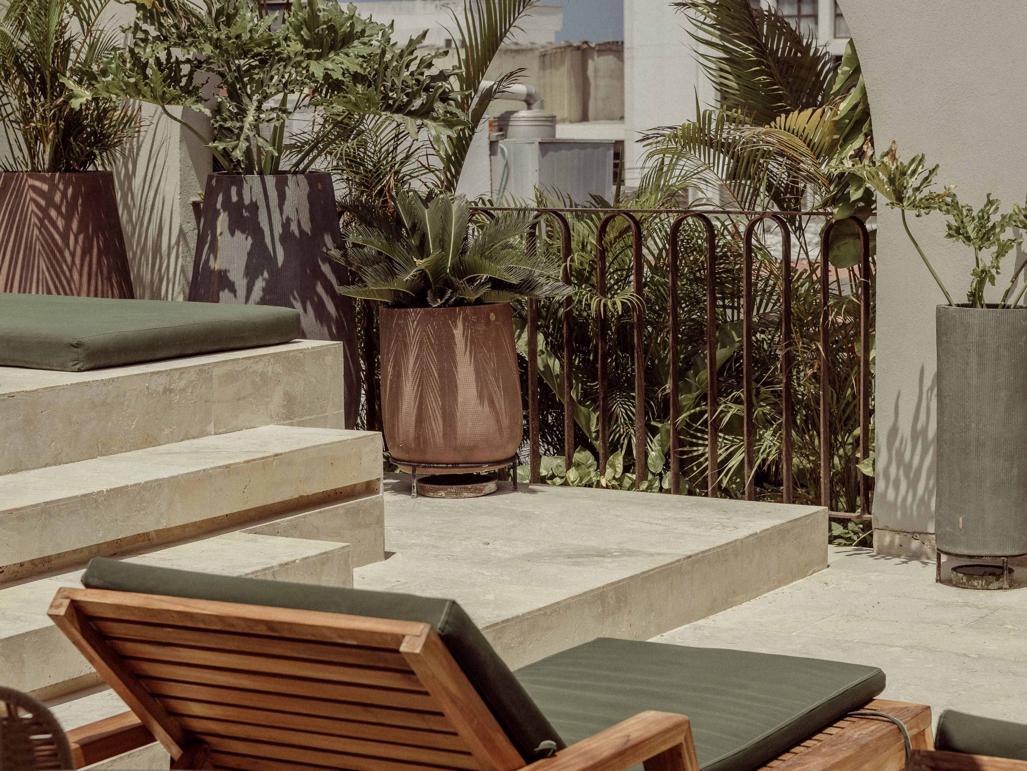 A rooftop terrace with concrete steps, wooden lounge chairs, and potted plants.