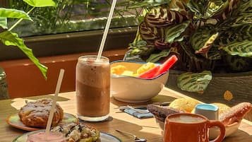 A breakfast table with various food items and drinks, set against a backdrop of lush green plants.