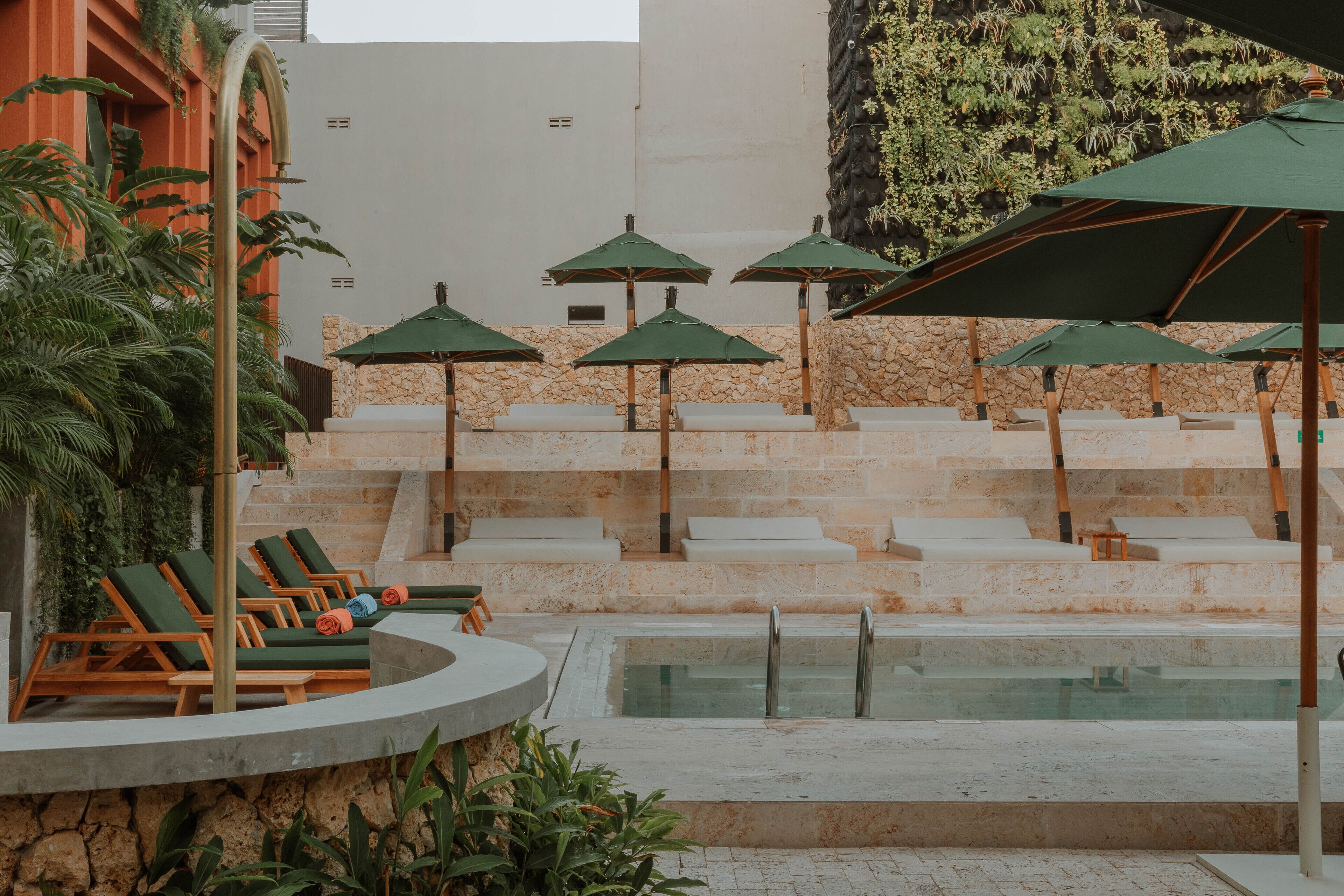 Zona de piscina con sillones de descanso y sombrillas, rodeada de escalones de piedra y vegetación.