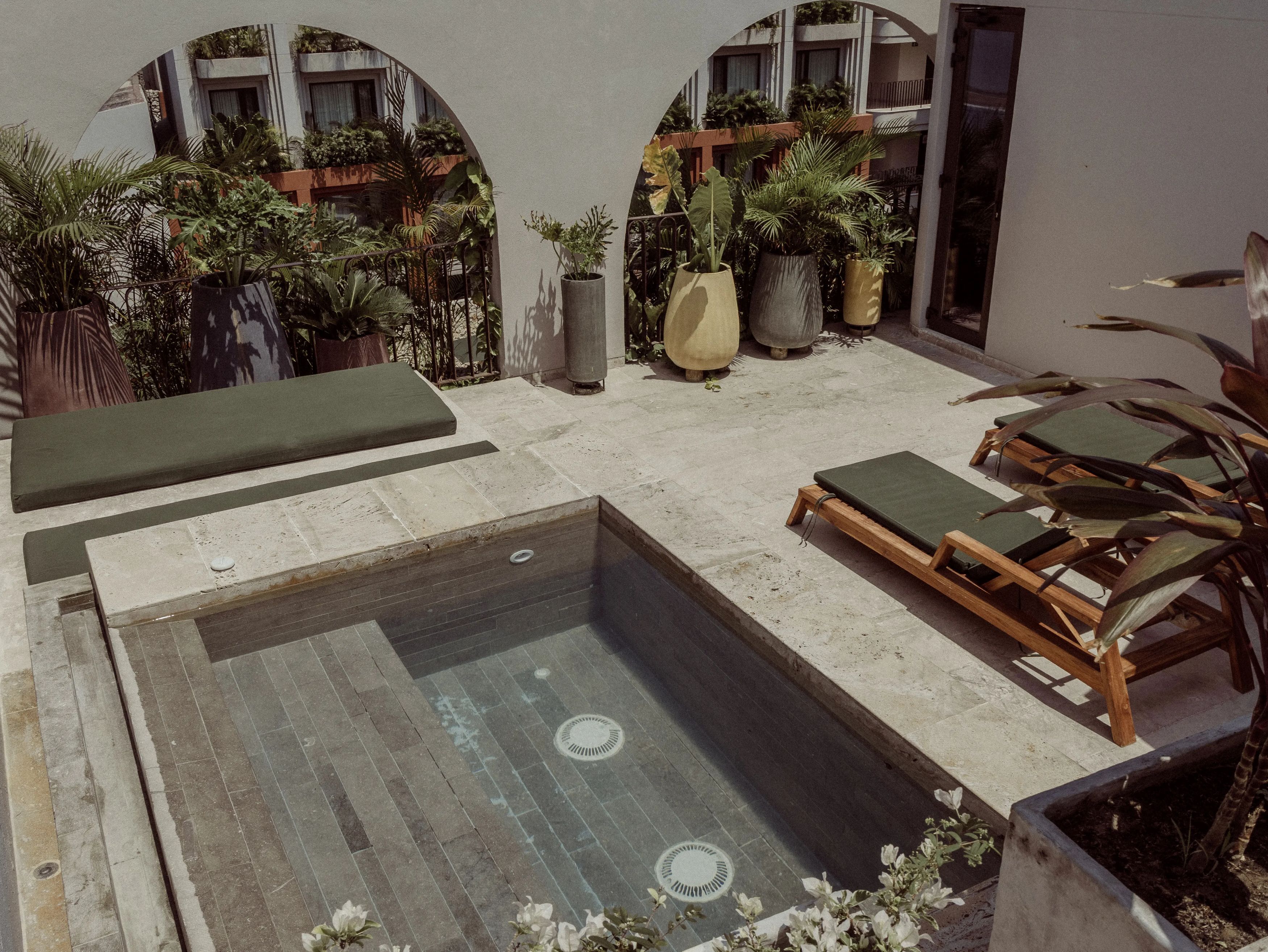 A rooftop terrace with a rectangular pool, lounge chairs, and potted plants.