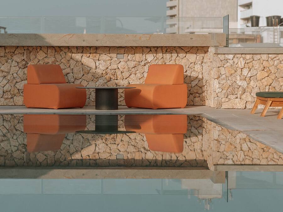 A rooftop pool area with stone walls, orange seating, and a clear view of the cityscape.