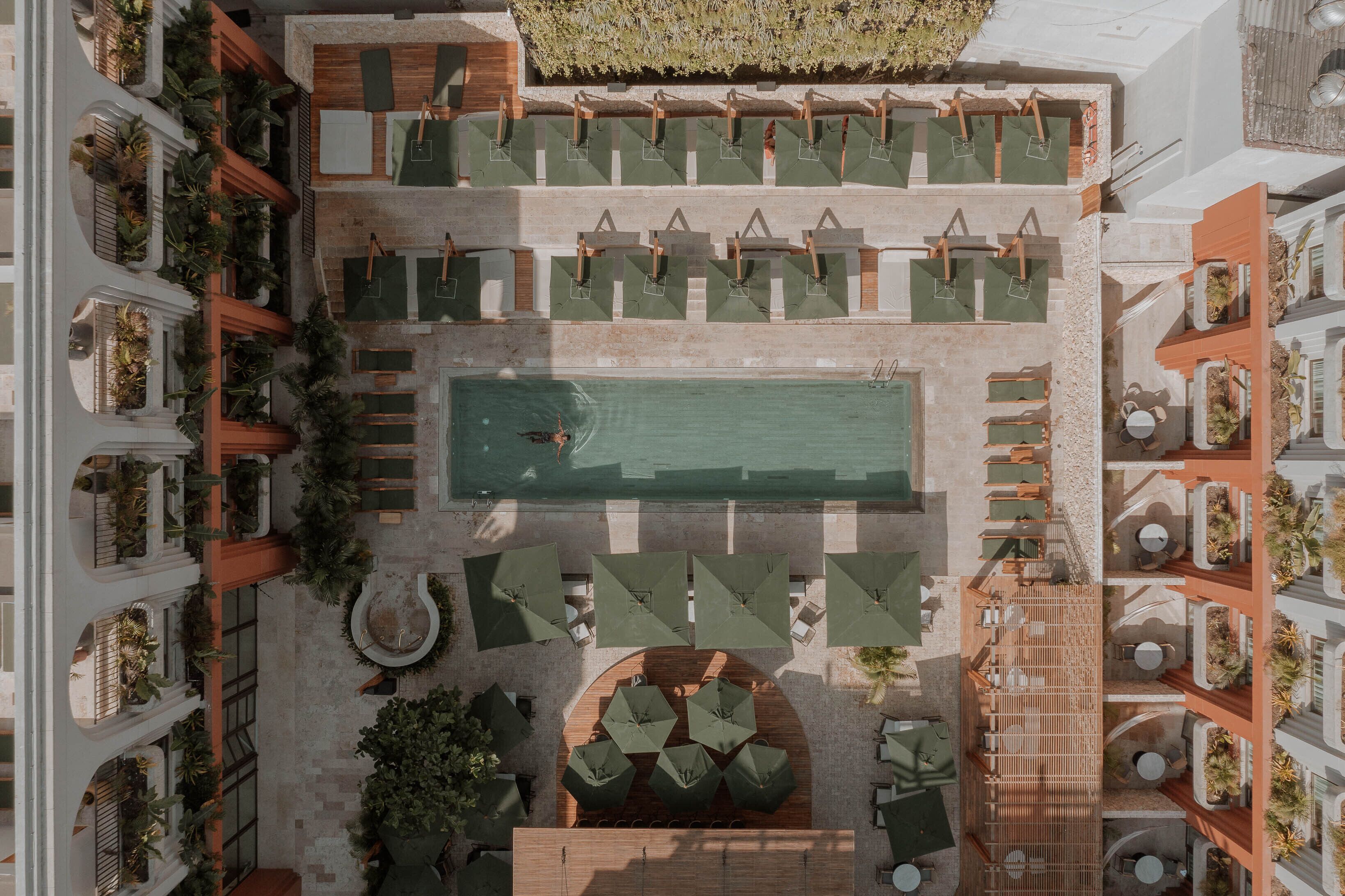 Vista aérea de un hotel con piscina central, zonas de estar al aire libre y balcones con plantas.