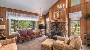 Un salon chaleureux aux murs en bois, doté d’une cheminée en pierre et d’une grande fenêtre donnant sur le paysage extérieur.