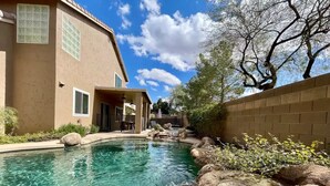 A swimming pool with rocks and a waterfall feature, surrounded by a house and trees. - Fantastic Family Fun 5BR w Pool/Spa in Gilbert (Gilbert)