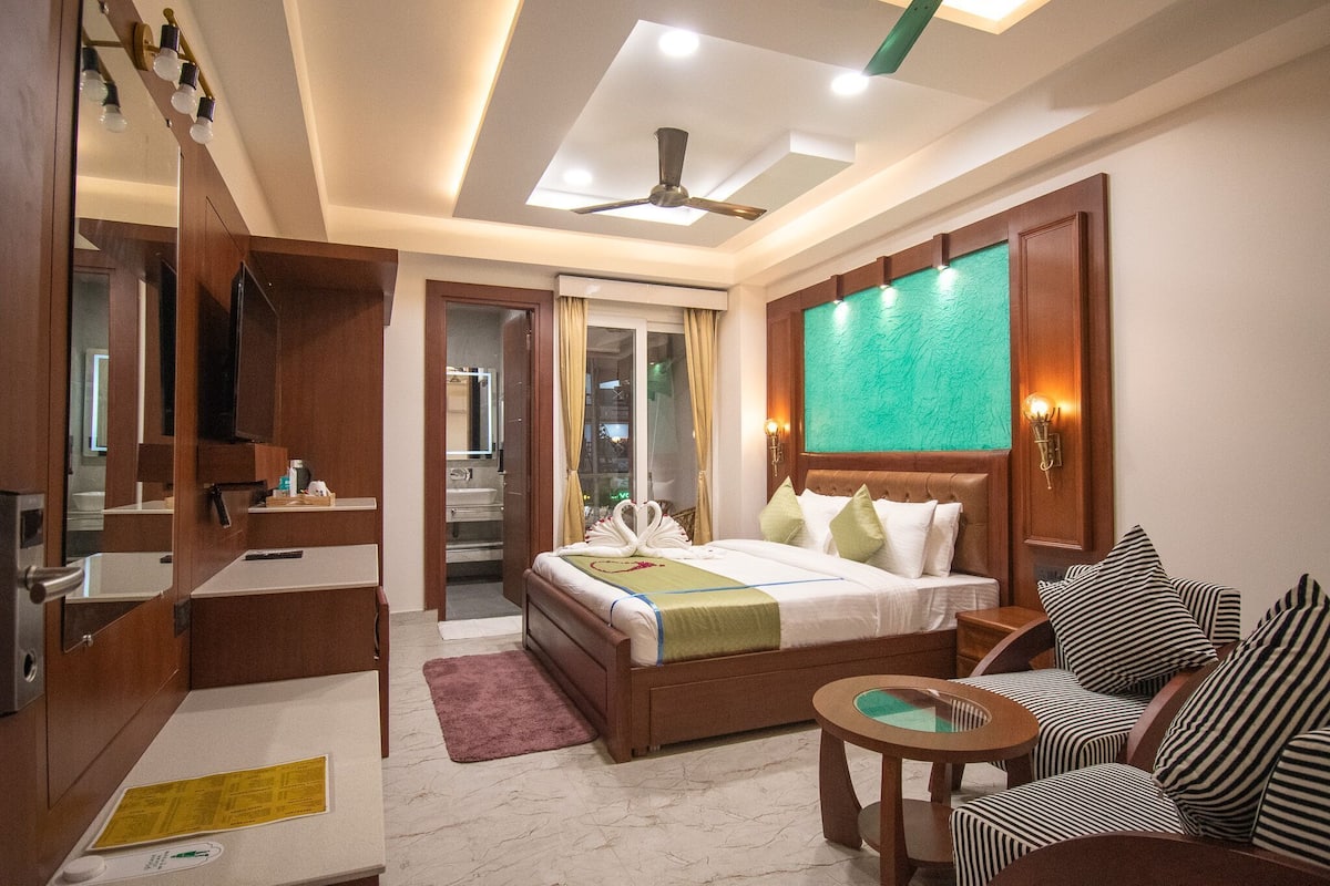 A hotel room with a bed, a seating area, a vanity, and a ceiling fan.