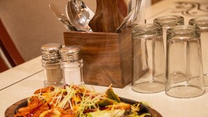 A wooden serving board with a vegetable and meat dish, salt and pepper shakers, and a set of cutlery in a wooden holder. - Holy Shivana Boutique Hotel Rishikesh (Narendranagar)